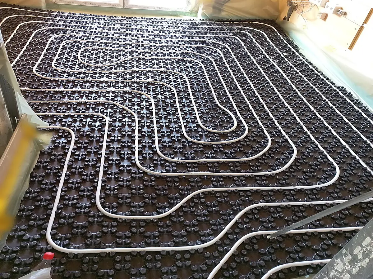 Plancher chauffant posé avant le coulage : panneau isolant à plots, tubes en serpentin, film et bande le long des murs