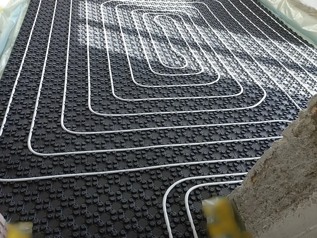 Tubes de plancher chauffant posés en serpentin sur un isolant à plots, prêts pour le coulage