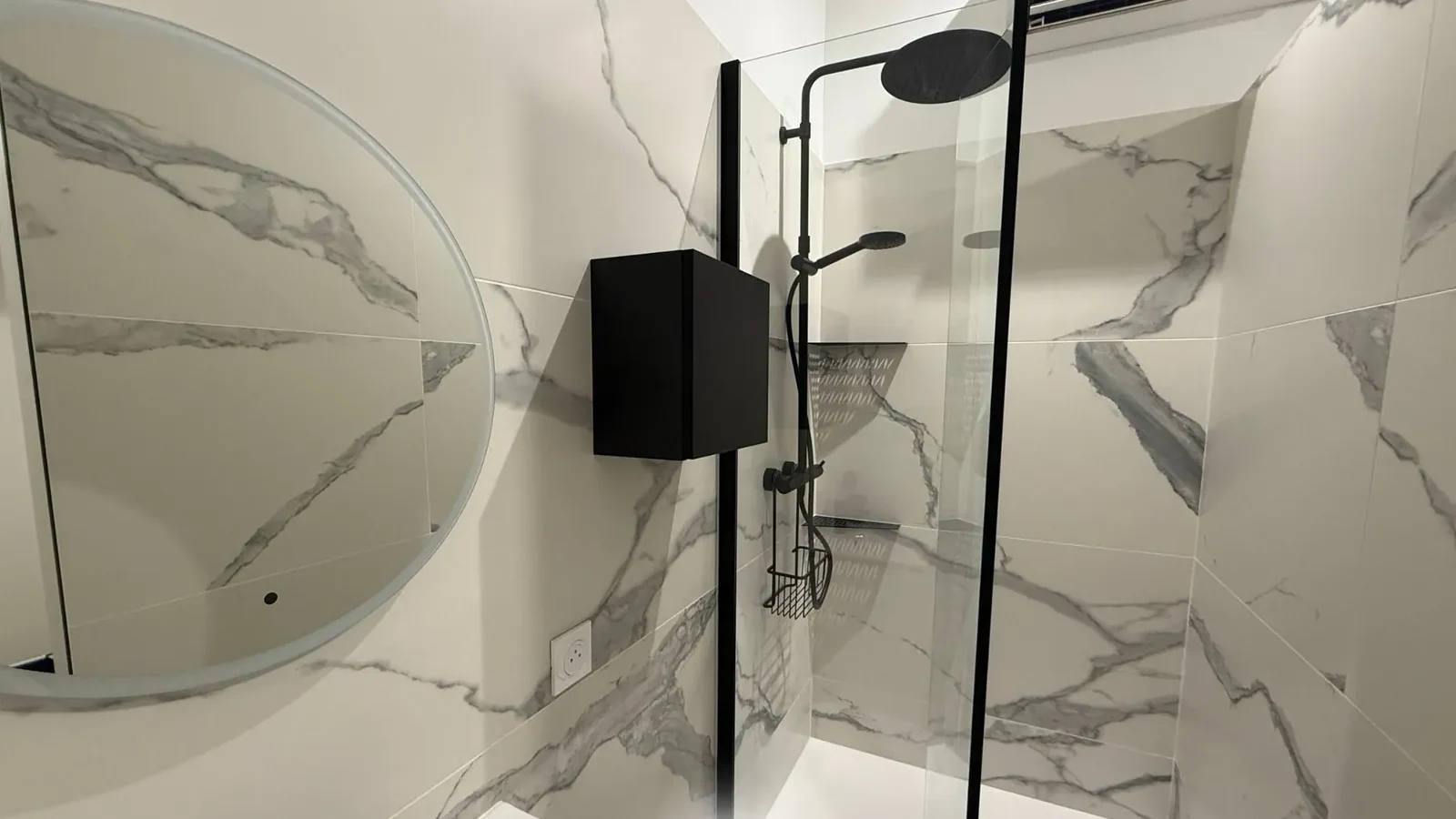 Petite salle de bain refaite : douche derrière une paroi fixe en verre, vasque compacte, faïence grand format effet marbre